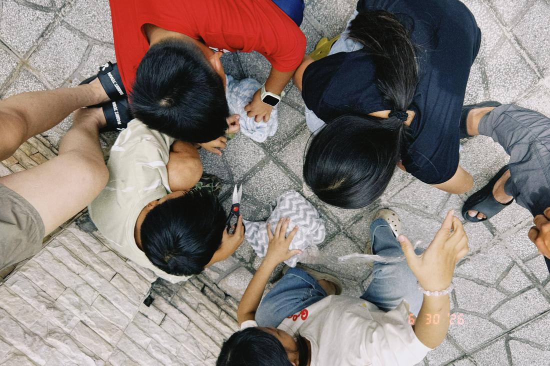 Overhead view of children and volunteers cutting fabric in a circle on a tiled courtyard.