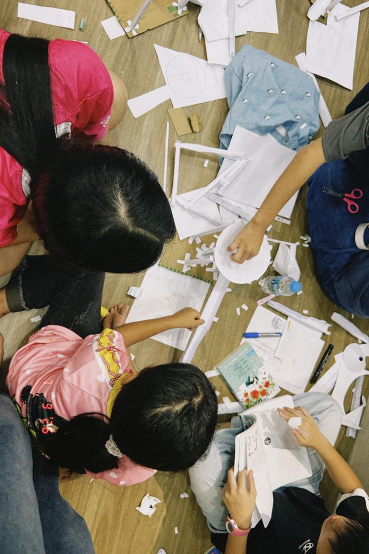 Overhead view of children building a paper roller-coaster from cut strips of paper.