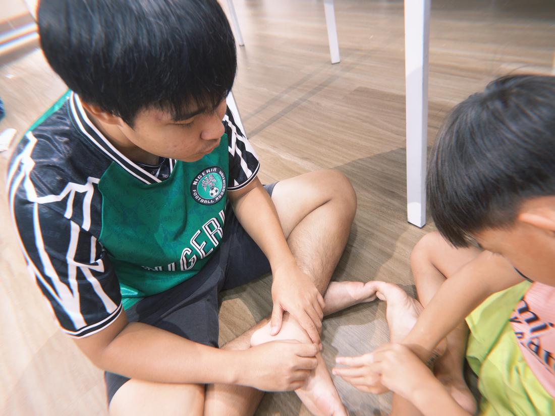 A Chạm volunteer sitting on the floor helping two children with an activity.